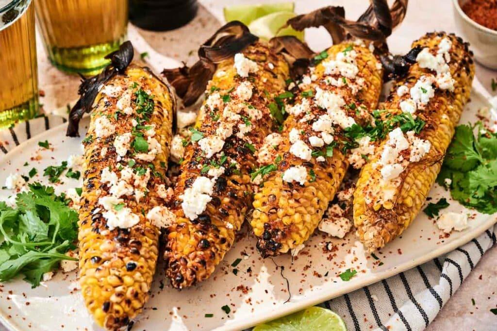 overhead shot of several grilled corn cobs arranged on a platter with lime wedges