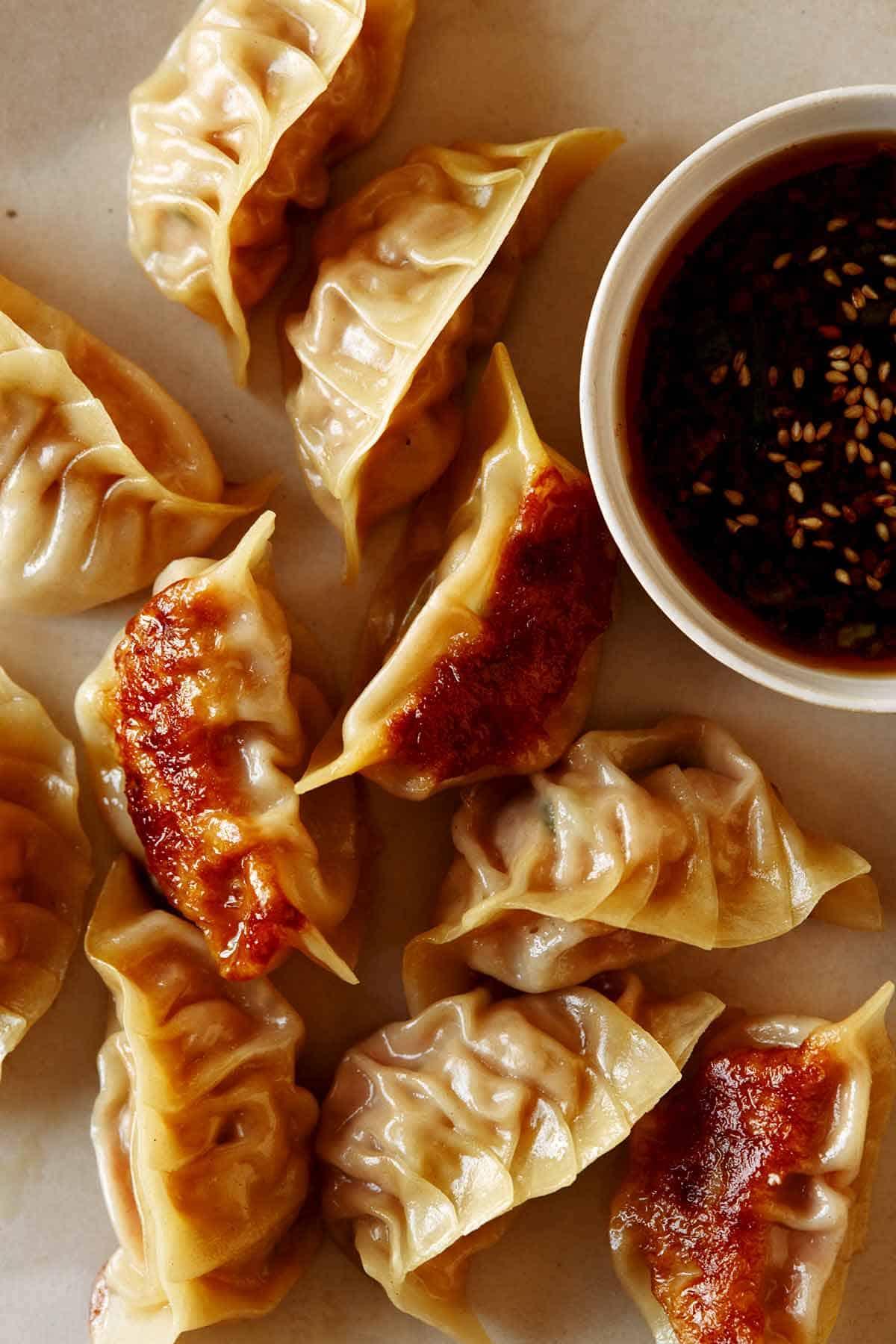 Close-up of a hand dipping a pulled pork potsticker into a small bowl of soy ginger glaze.