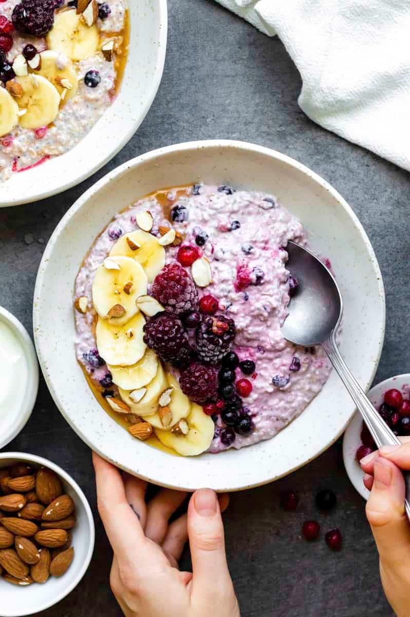 A person preparing overnight oats in a kitchen, adding fruit