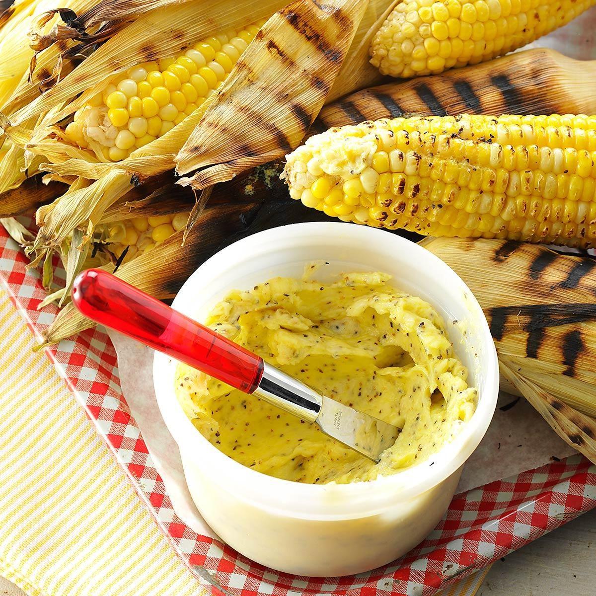 person spreading lemon-pepper butter on grilled corn