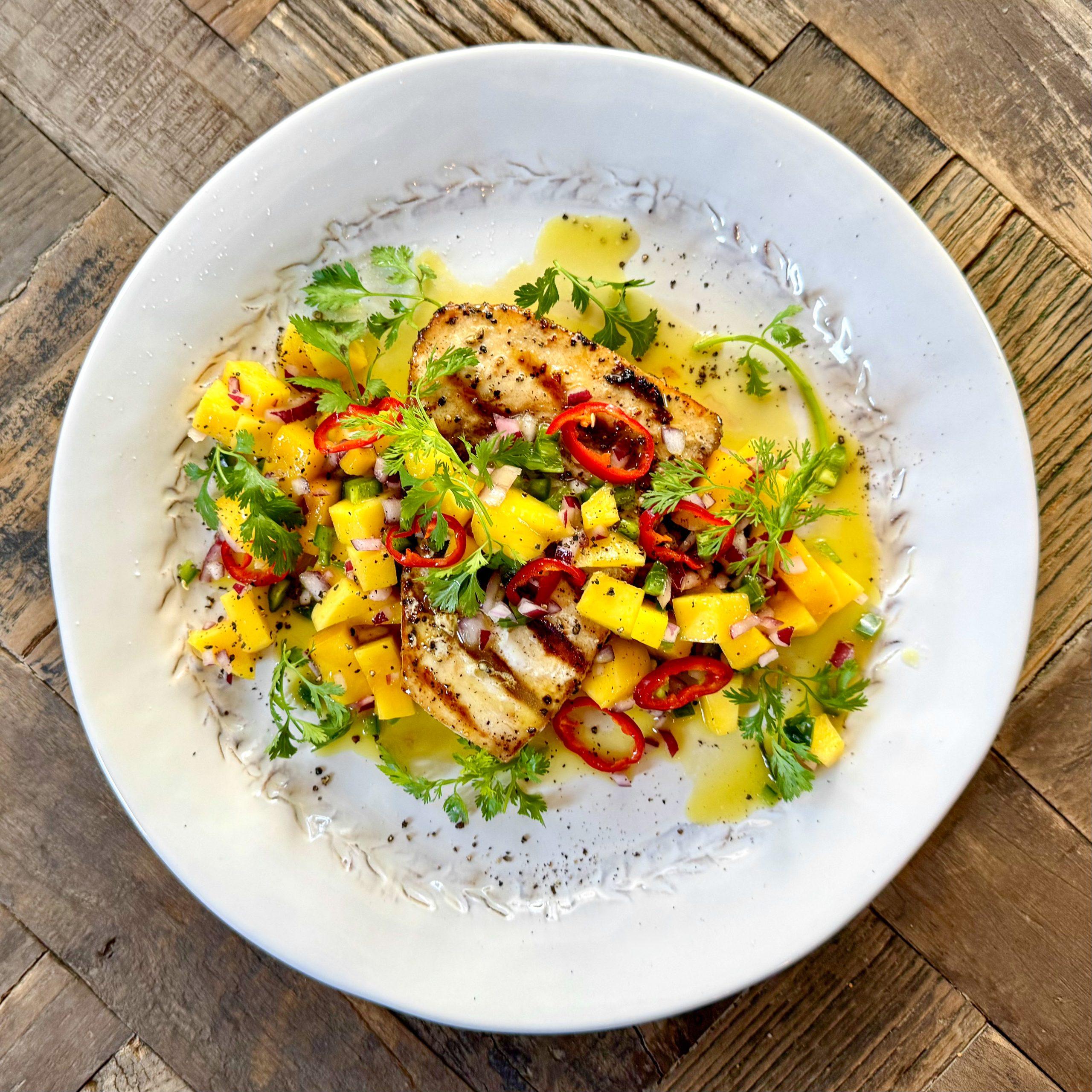 completed grilled swordfish with mango salsa on a plate, garnished with lime wedges