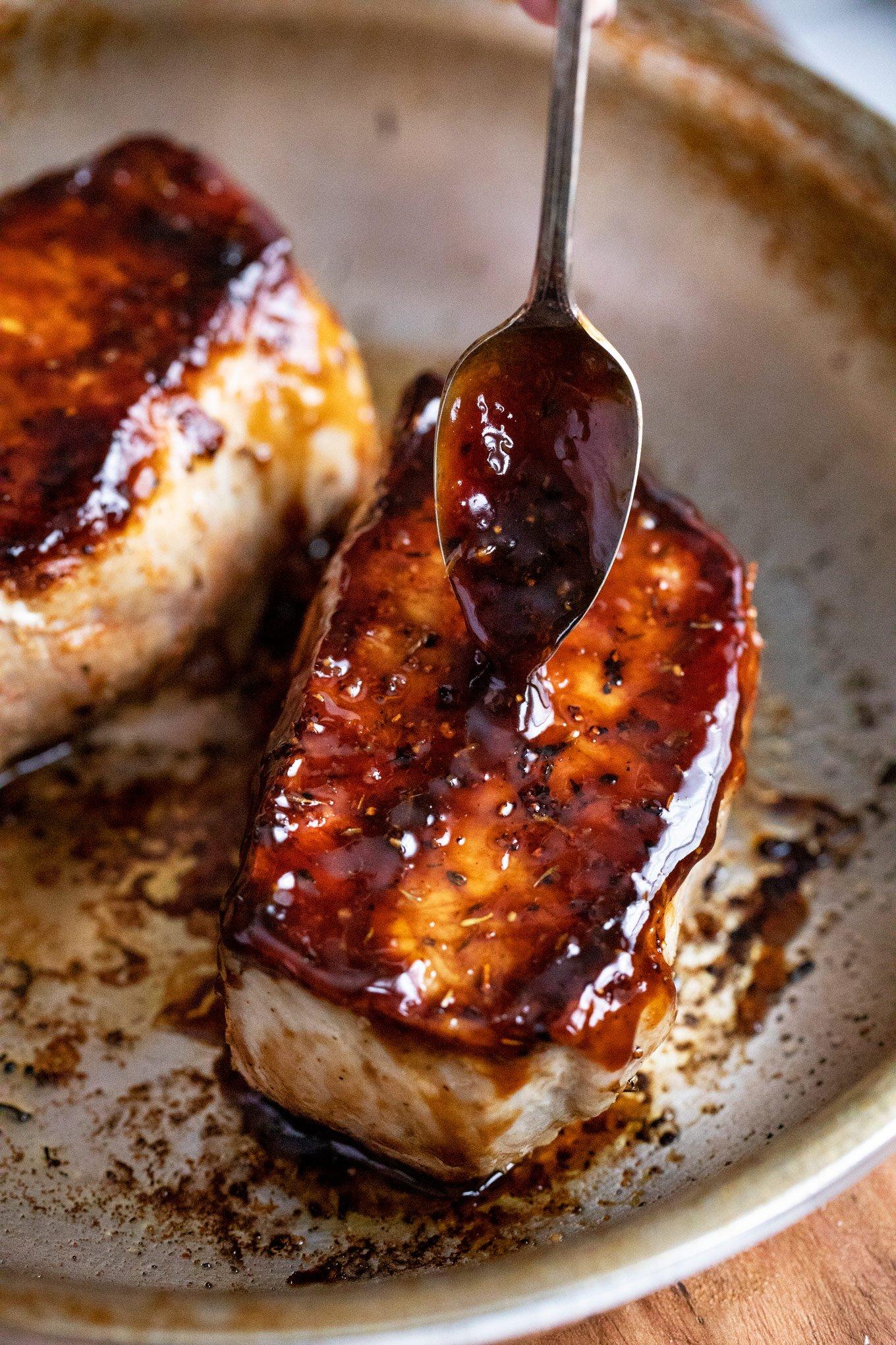 pork chops being glazed with bourbon sauce using a brush