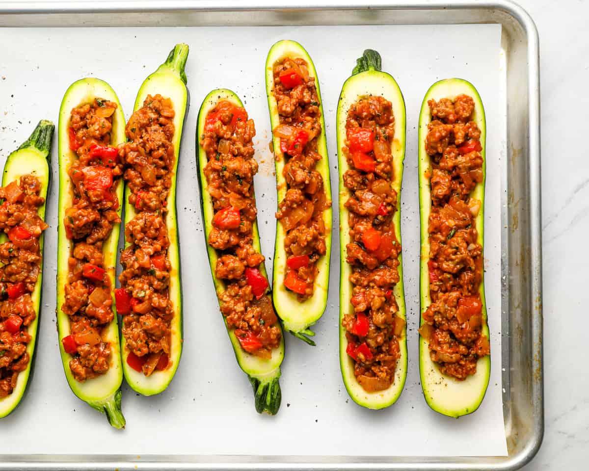 Stuffed zucchini boats arranged on a baking sheet, ready to go into the oven