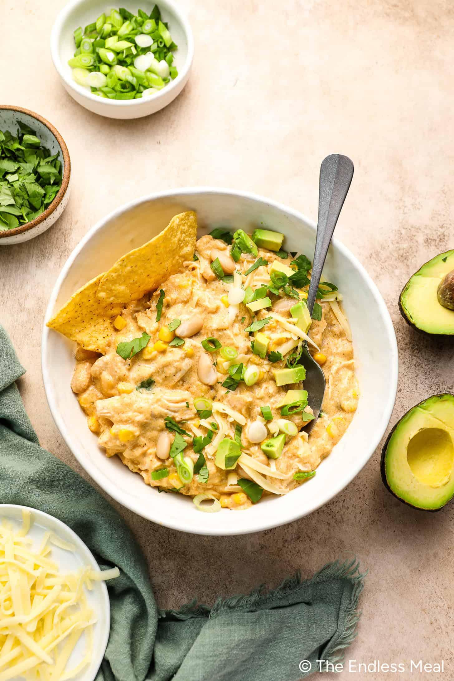 A rustic bowl of zesty white chicken chili, topped with fresh cilantro and avocado slices, steaming, in a cozy setting.