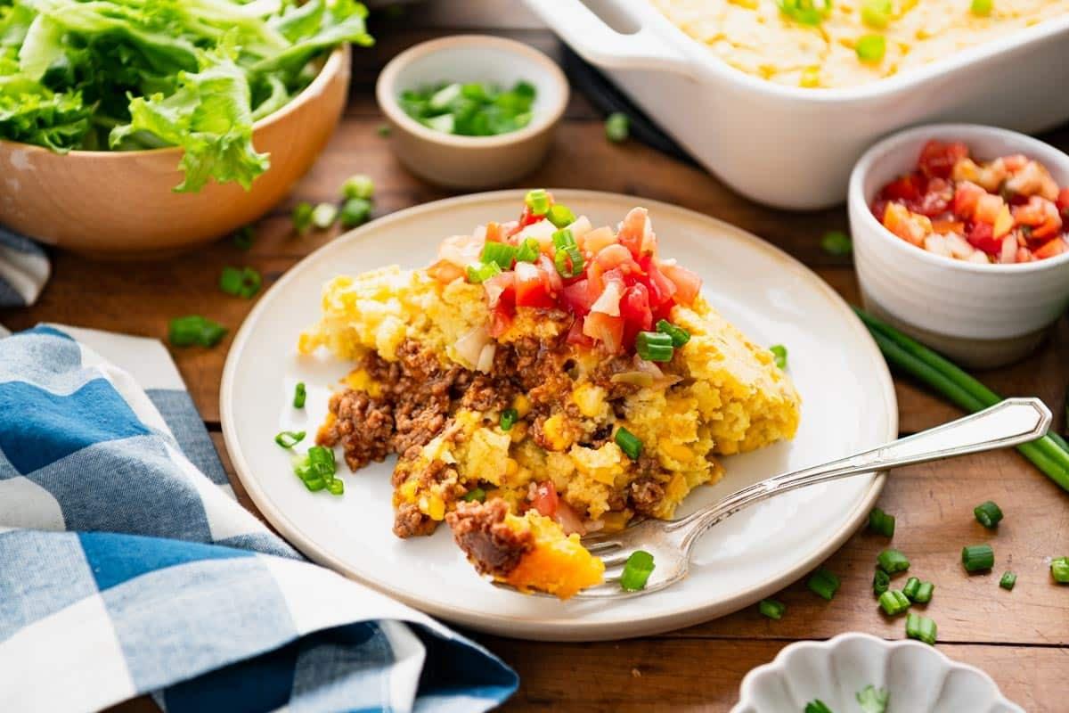 slices of beefy cornbread casserole on plates, garnished with fresh herbs
