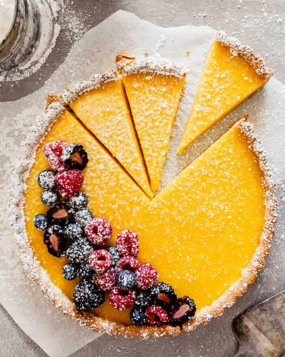 a whole lemon curd raspberry tart on a fluted tart pan, dusted with powdered sugar