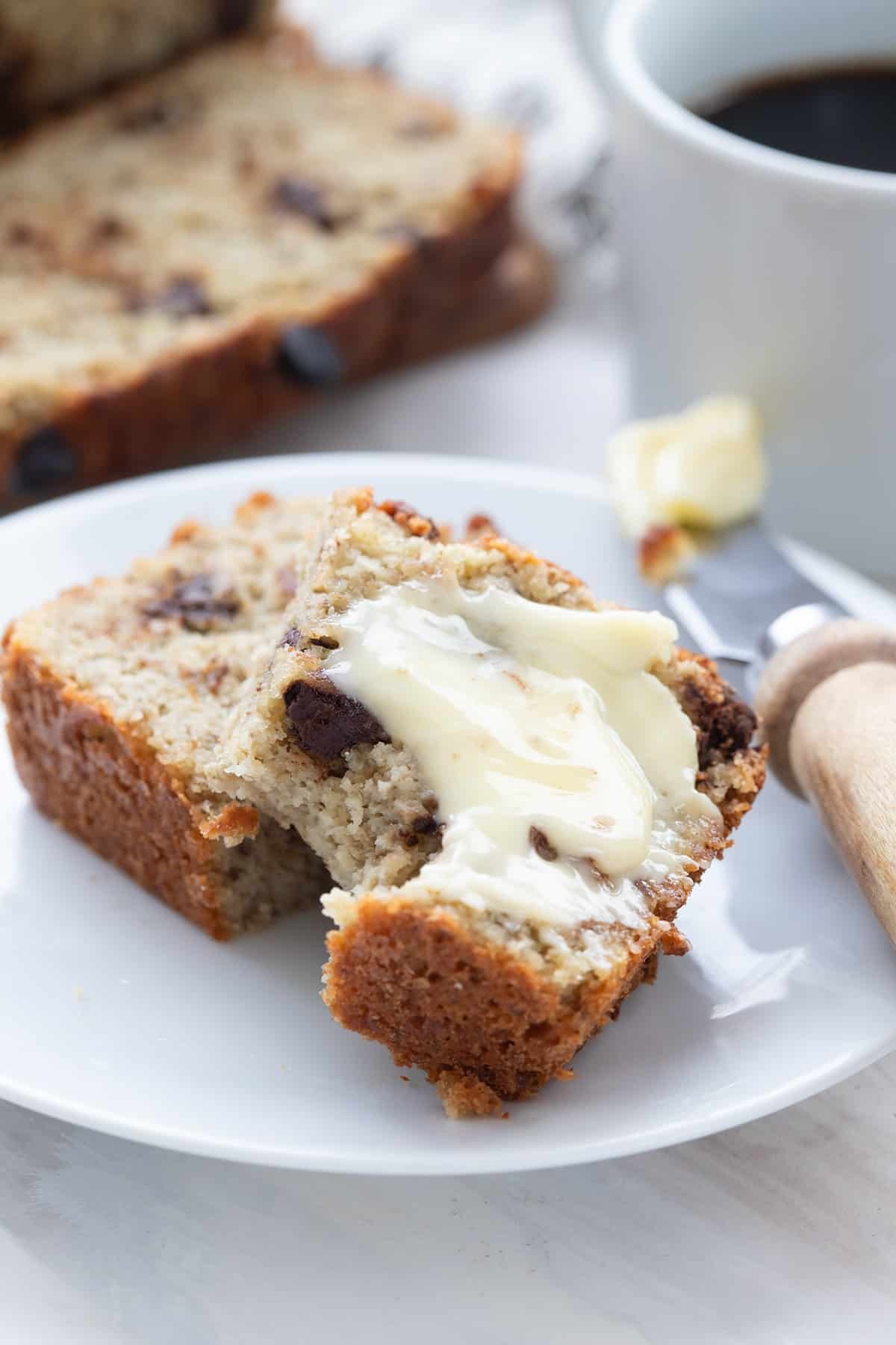 slices of keto banana bread on a white plate, with a cup of coffee