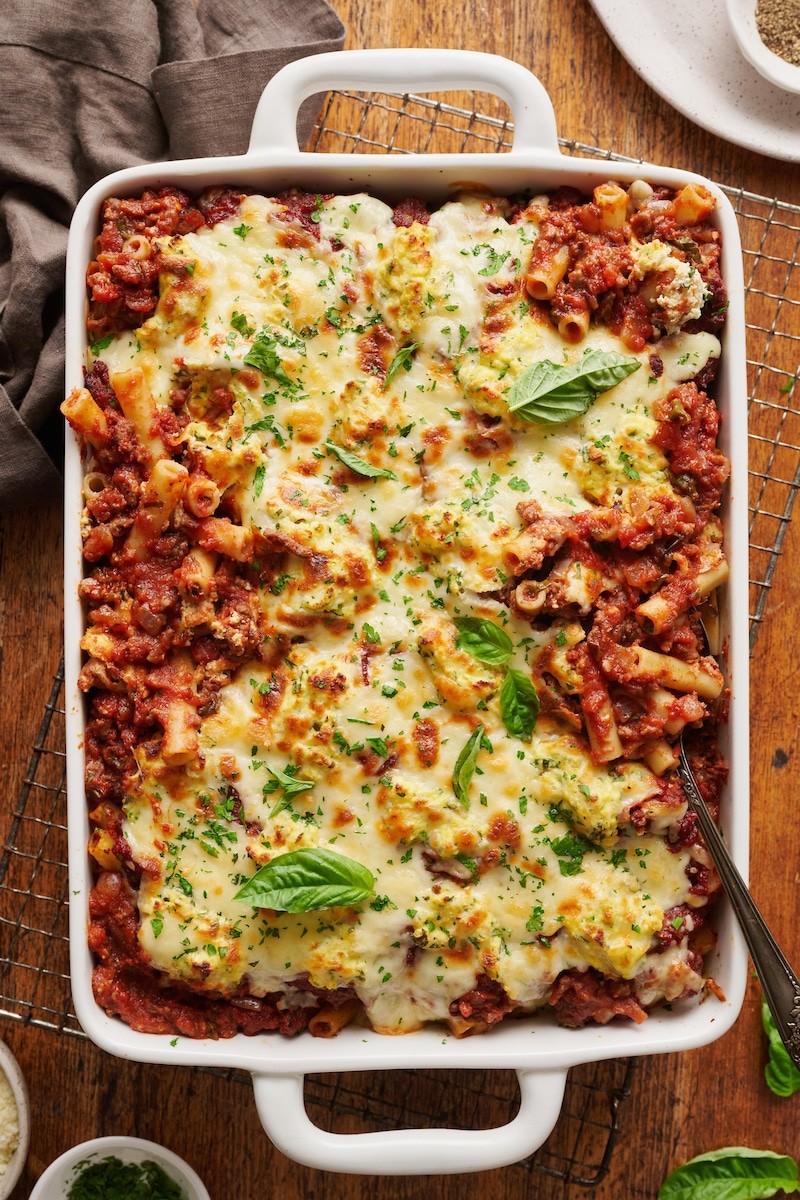 Hearty cheesy baked ziti bubbling in a ceramic baking dish, garnished with fresh basil