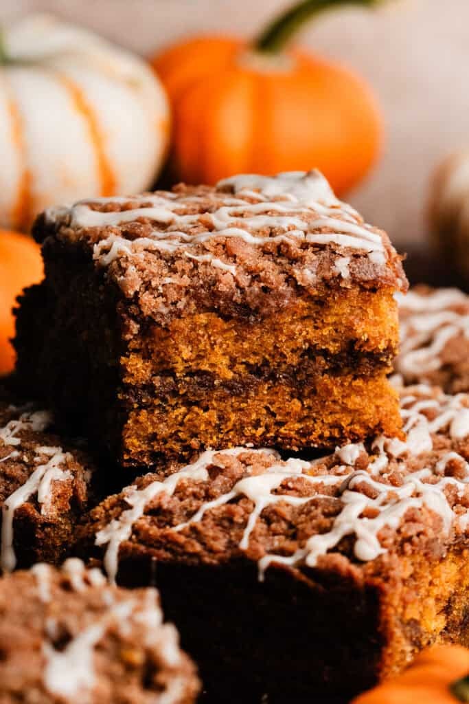 pumpkin coffee cake with a dusting of powdered sugar on a wooden table, autumn leaves scattered around