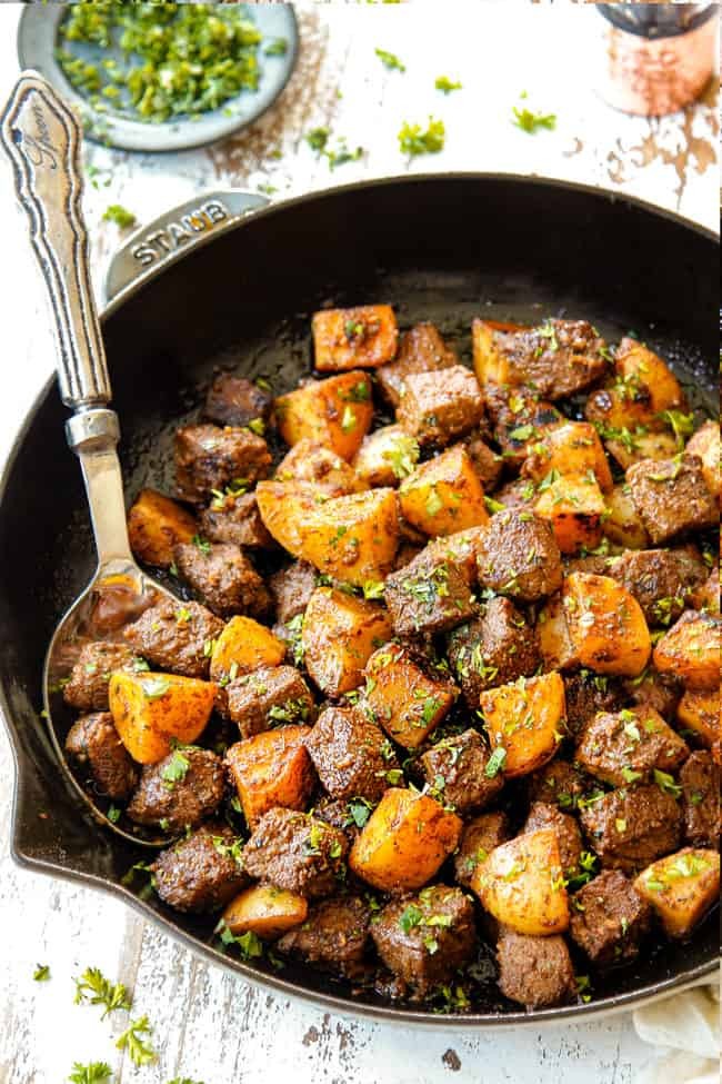 Rustic cast iron pan with garlic butter beef and tender potatoes, garnished with fresh parsley