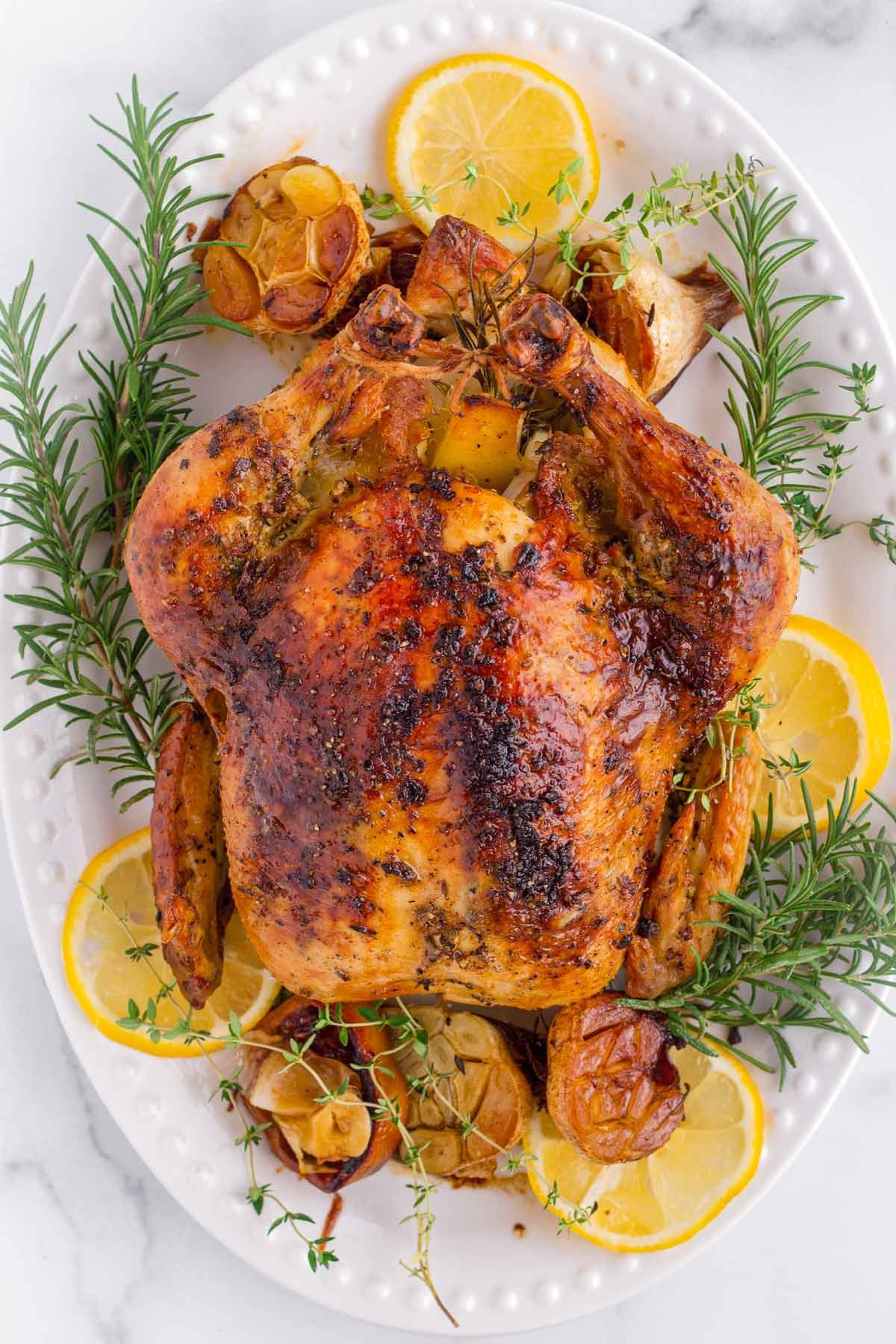 golden brown whole roasted chicken on a platter with herbs
