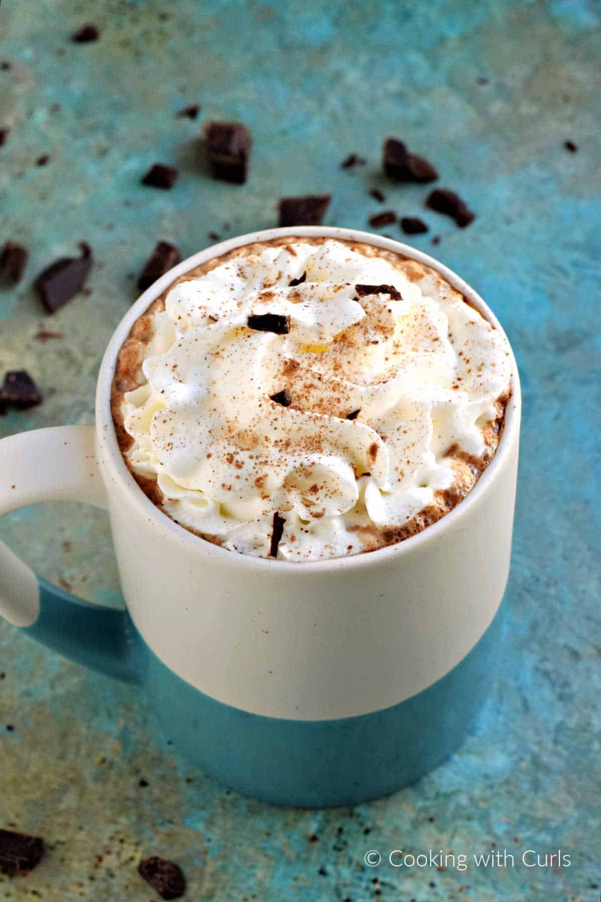 Steaming mug of rich mocha hot chocolate with whipped cream and chocolate shavings, cozy setting