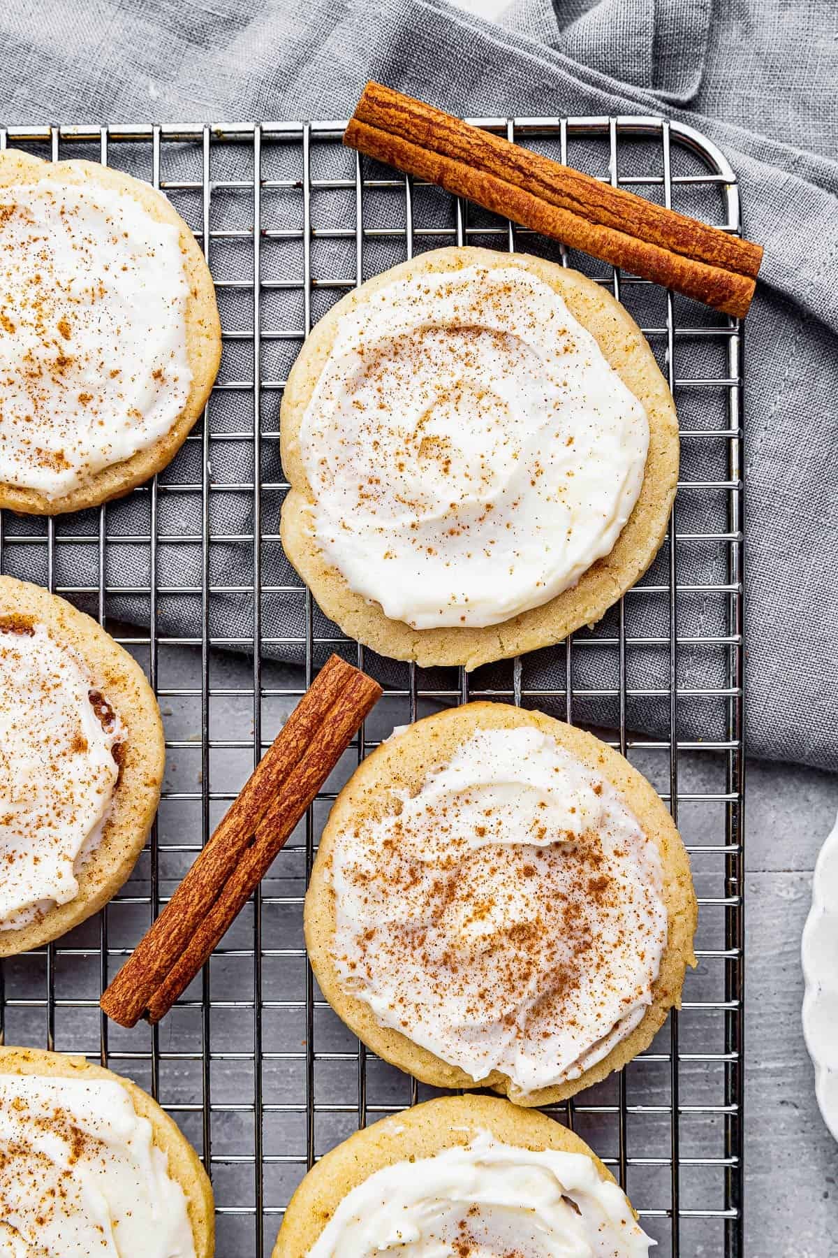 Close-up of freshly baked sugar cookies with vanilla frosting swirls on a cooling rack, cozy kitchen background