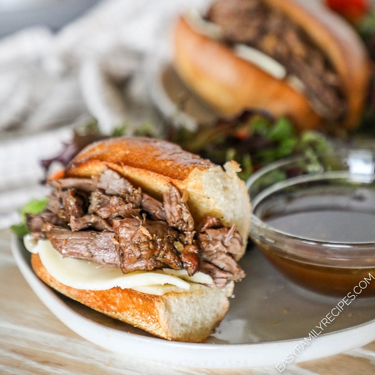 close-up of crockpot french dip sandwiches with a rich, dark au jus dipping bowl