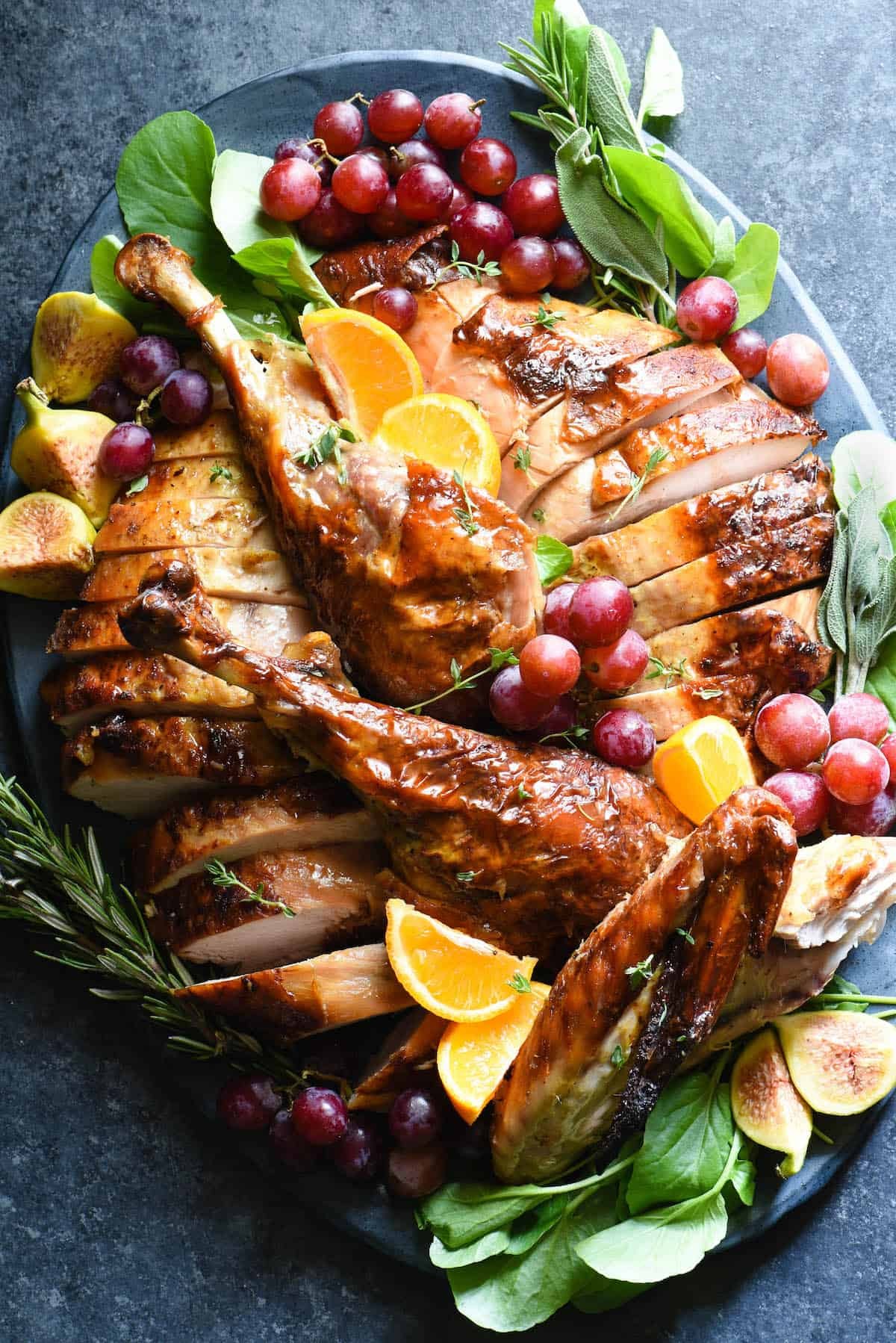 Beautifully roasted maple glazed turkey with citrus slices and herbs on a platter, ready to be served at a holiday table