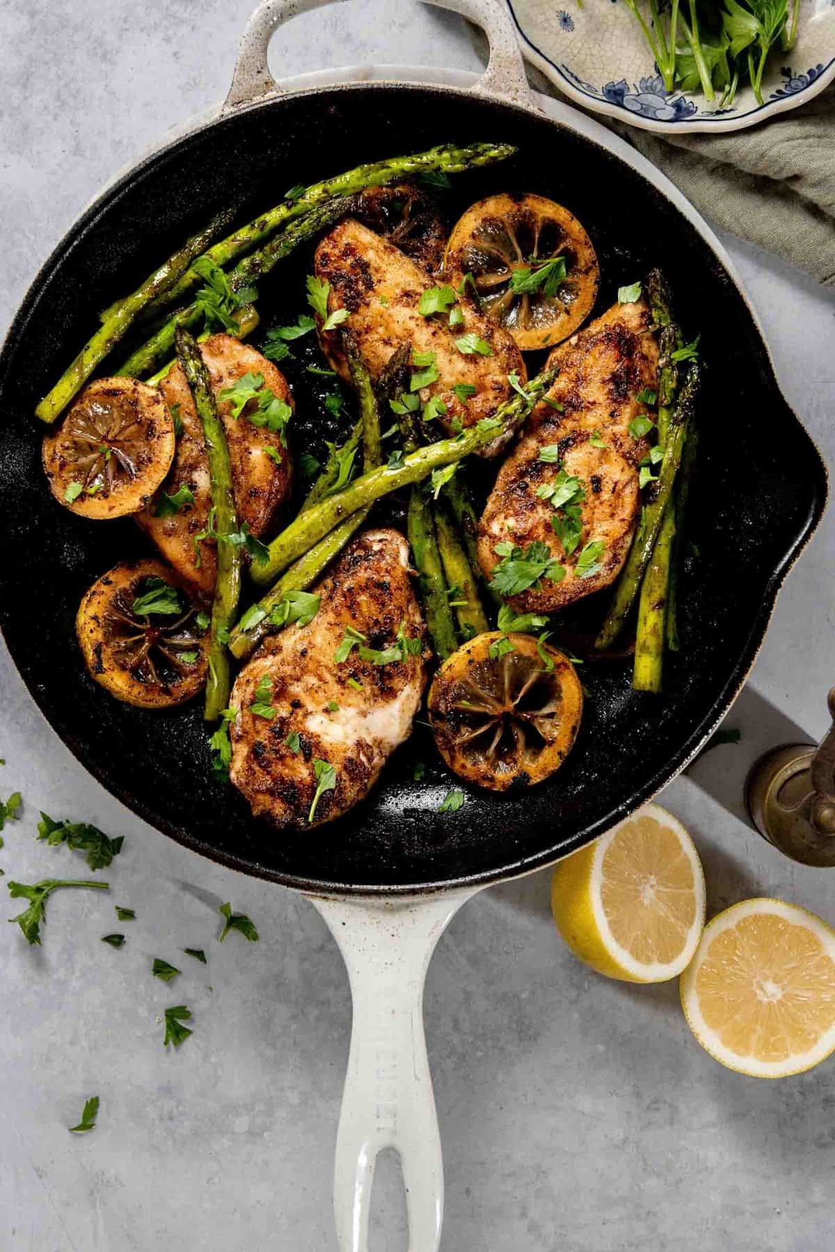 Golden brown pan-seared lemon chicken breasts with fresh herbs and lemon slices in a skillet