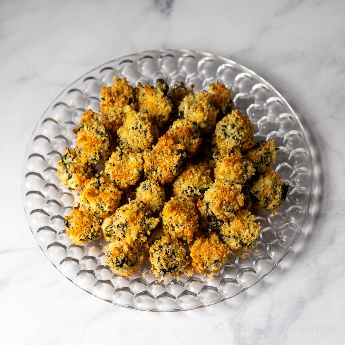 Platter of golden brown mini spinach artichoke dip bites with fresh parsley garnish on a festive party table