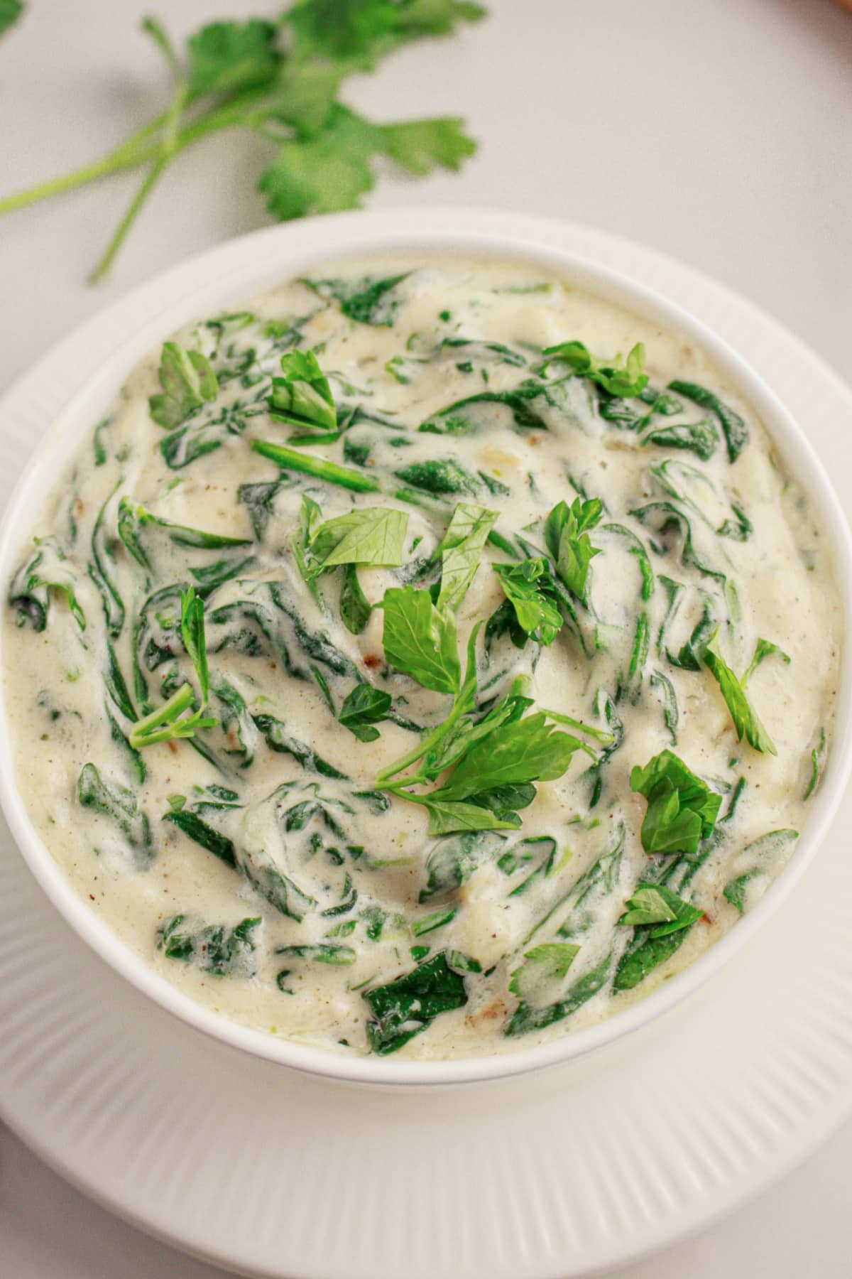 Creamed spinach in a white ceramic bowl, garnished with fresh parsley, rich and creamy texture