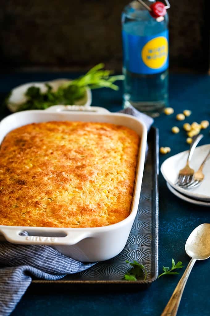 Southern corn casserole with golden-brown crust, steaming hot, on a rustic wooden table with a side of greens