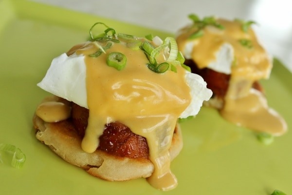 close up of a pork and bacon benedict with hollandaise sauce dripping