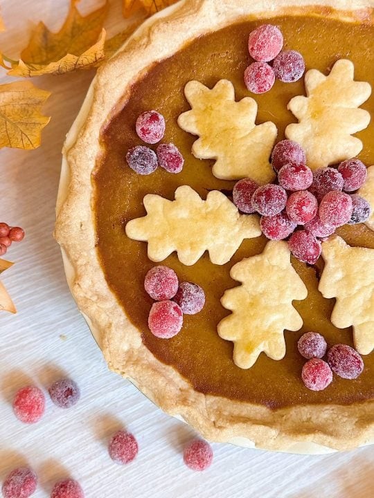 Homemade brown sugar pumpkin pie with a golden crust, surrounded by autumn leaves and warm spices like cinnamon sticks and star anise, rustic setting