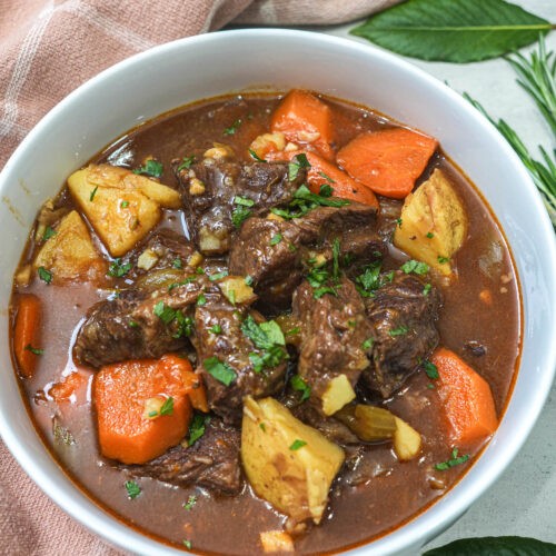 hearty crockpot beef stew with tender chunks of beef, potatoes, carrots, and celery, garnished with fresh parsley, steaming bowl, rustic wooden table