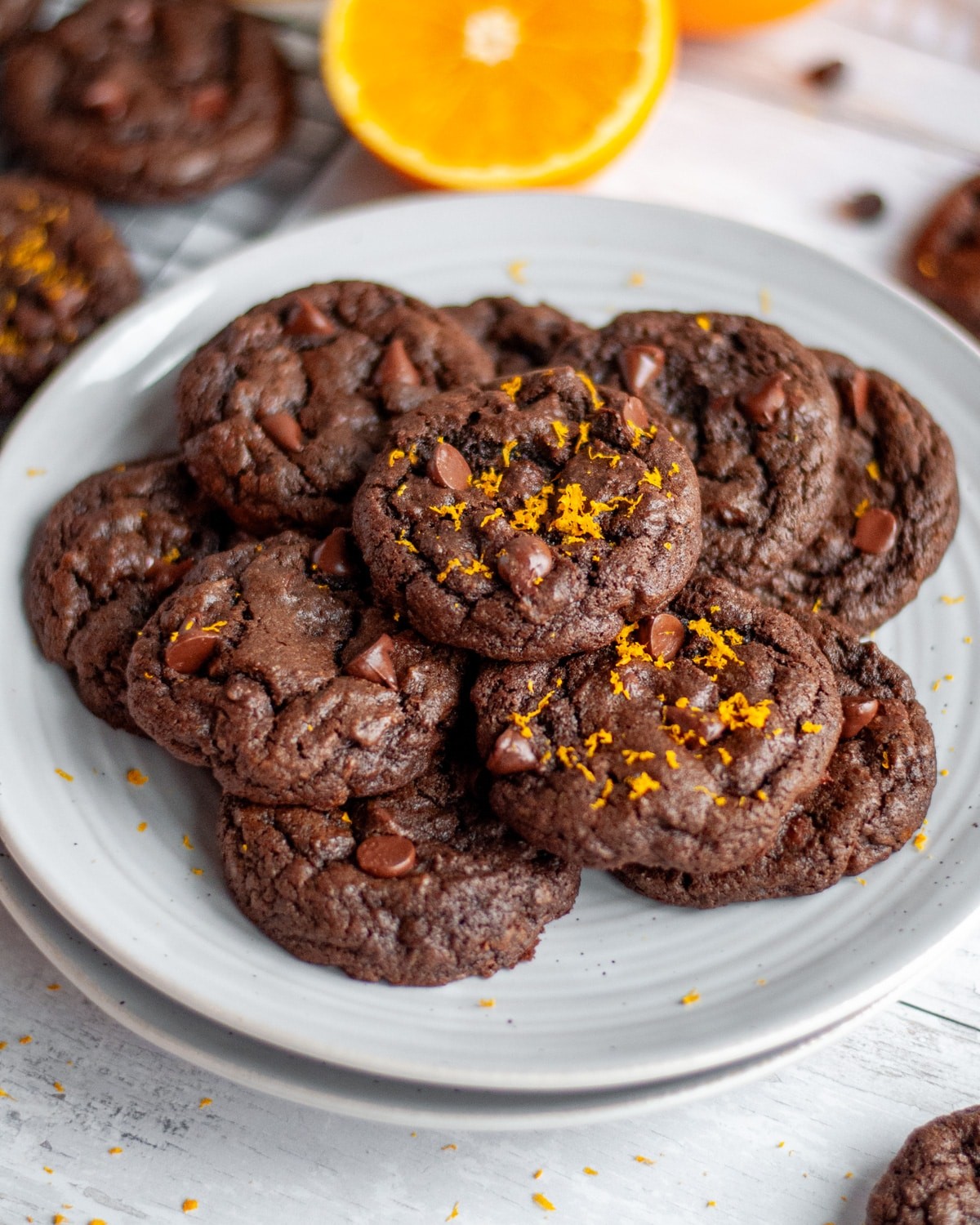Vibrant close-up of glossy chocolate orange cookies stacked on a cooling rack, with fresh orange zest scattered nearby