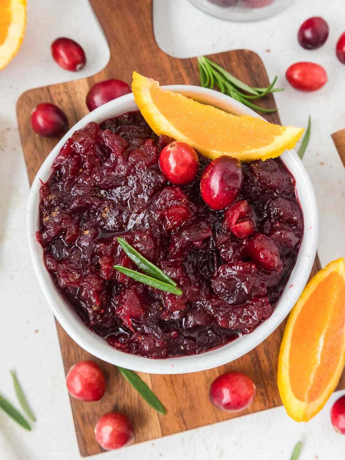 Vibrant homemade whole berry cranberry sauce in a decorative bowl with fresh orange slices and cranberries scattered around, festive background
