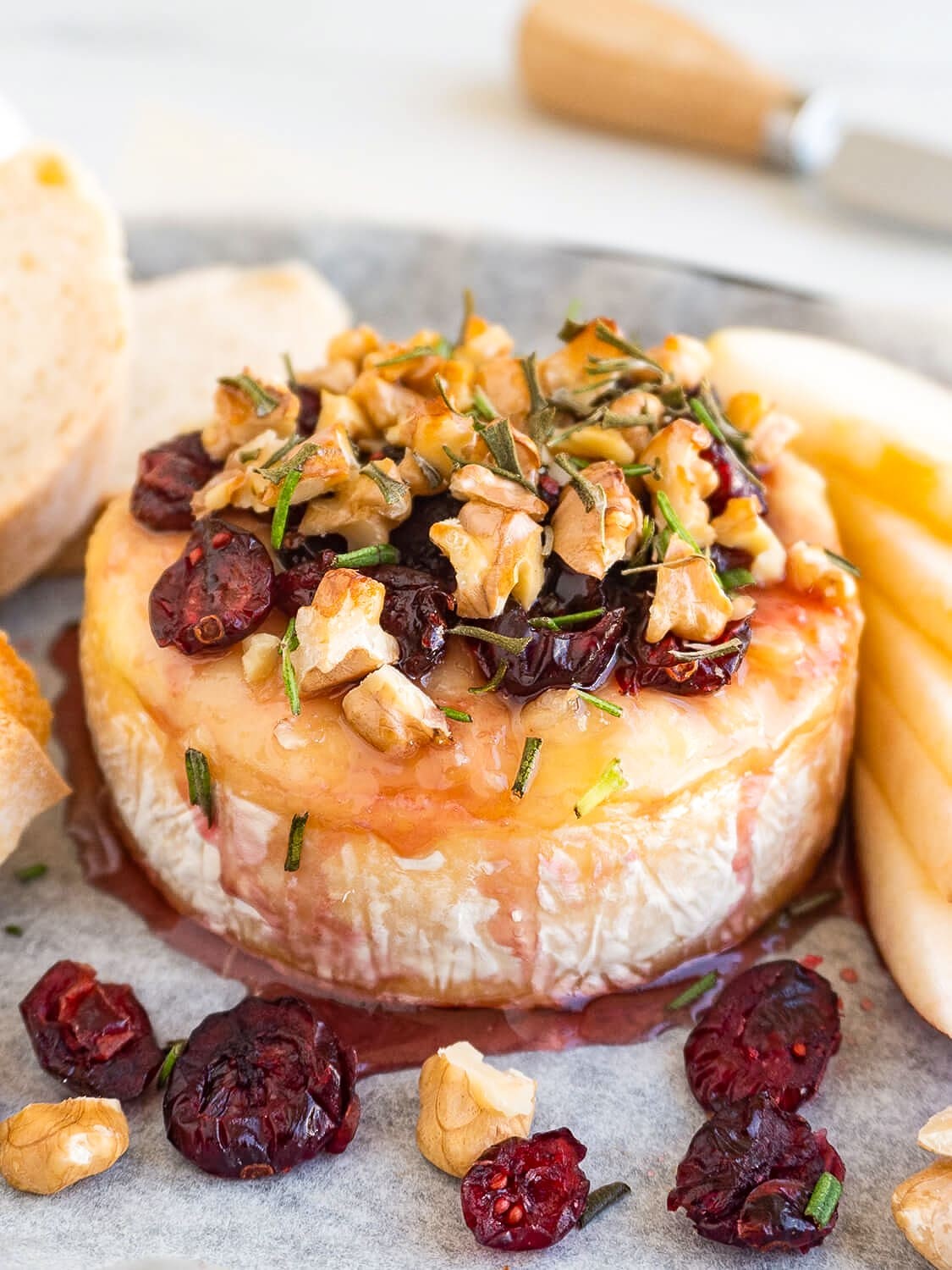 Gourmet baked brie wheel drizzled with golden honey, scattered walnuts and dried cranberries, served with toasted baguette slices on a rustic wooden board, warm and inviting atmosphere.