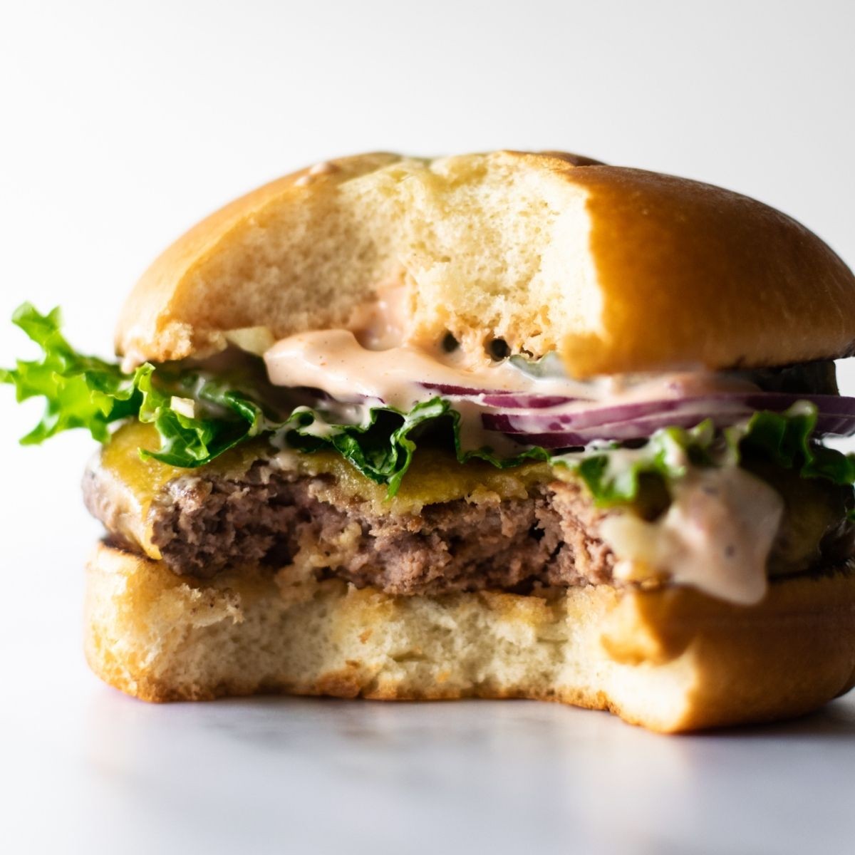 Delicious smash burger with melted cheese and vibrant secret sauce oozing out, served on a toasted brioche bun with crispy edges.