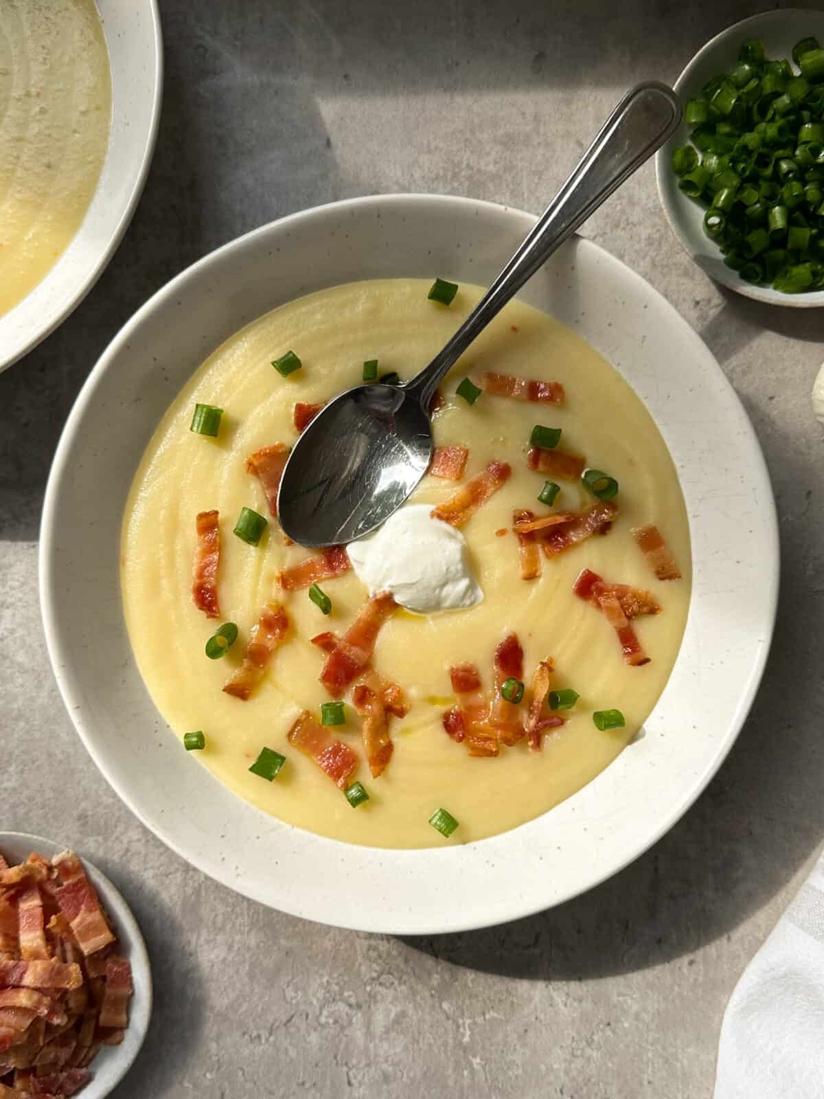 Delicious creamy potato soup with crispy bacon bits and fresh green scallions on top, rustic bowl, cozy setting