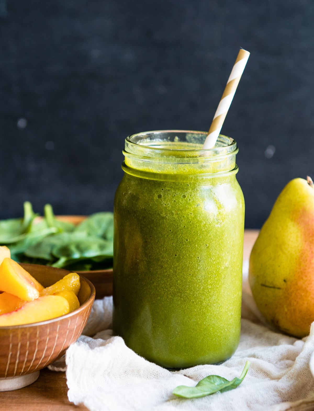 vibrant pear smoothie in a glass with fresh pears and spinach around it