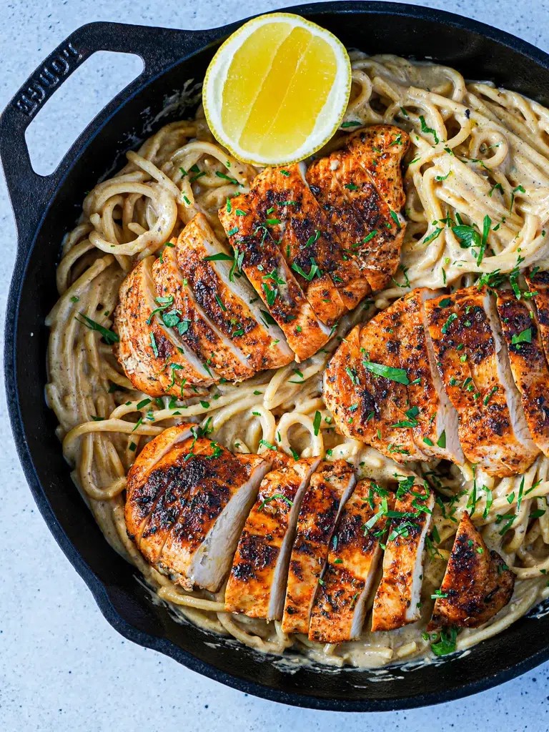 Creamy lemon chicken breast with pasta and fresh herbs, close-up, warm lighting