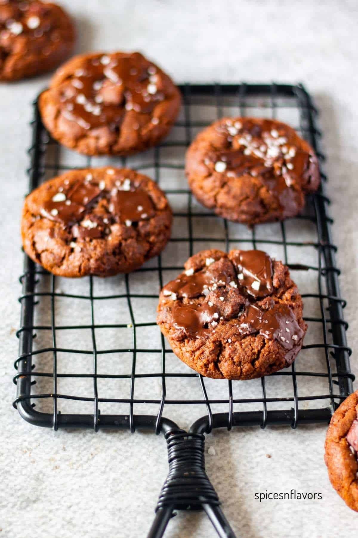 Dark chocolate espresso cookies on a cooling rack, garnished with coffee beans, rich dark background