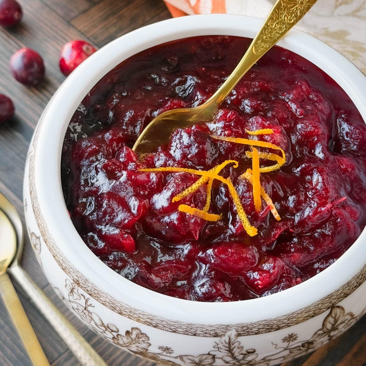 Close-up of a rustic bowl of homemade cranberry sauce with orange zest and cinnamon sticks, with autumn decor in background