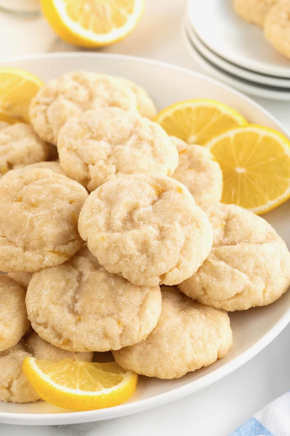 Platter of freshly baked lemon zest cookies with powdered sugar and lemon slices, warm kitchen lighting