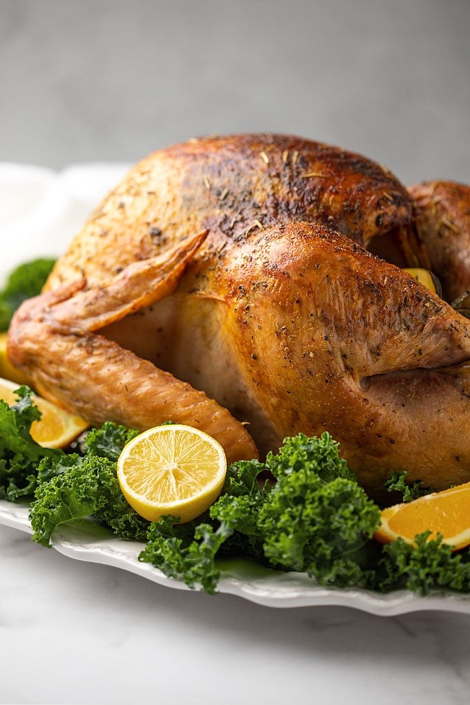 Whole roasted butter basted turkey with crispy crackling golden skin on a platter, garnished with herbs and roasted vegetables