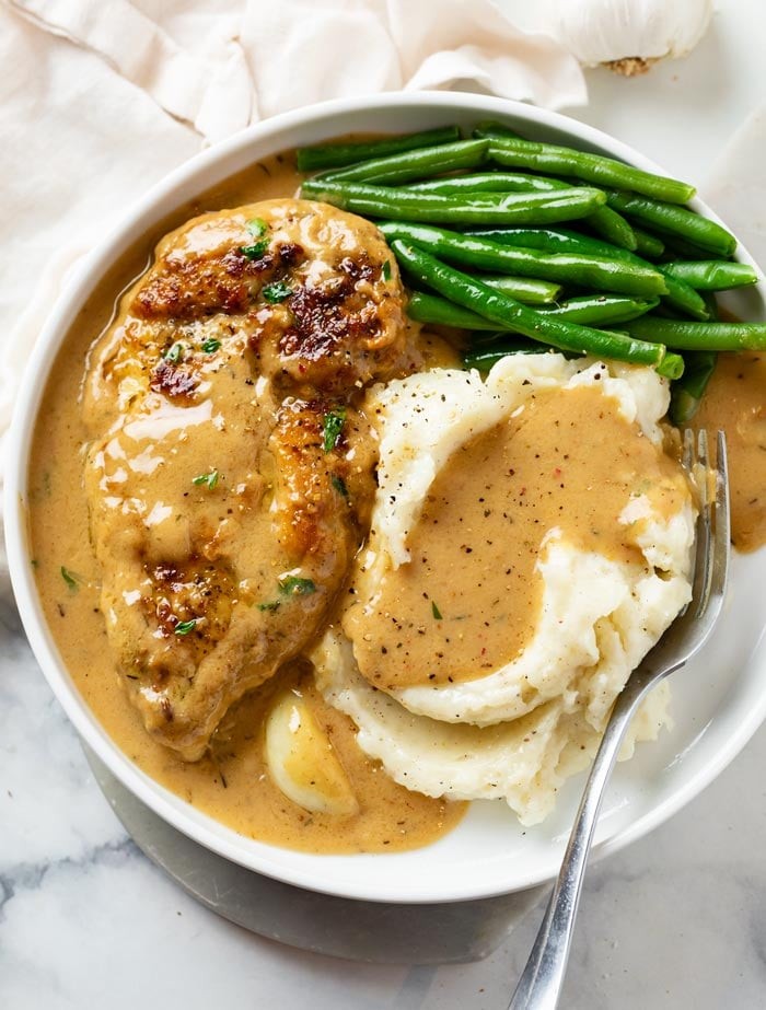 overhead shot of creamy white garlic chicken in a crockpot with parsley garnish, served with mashed potatoes