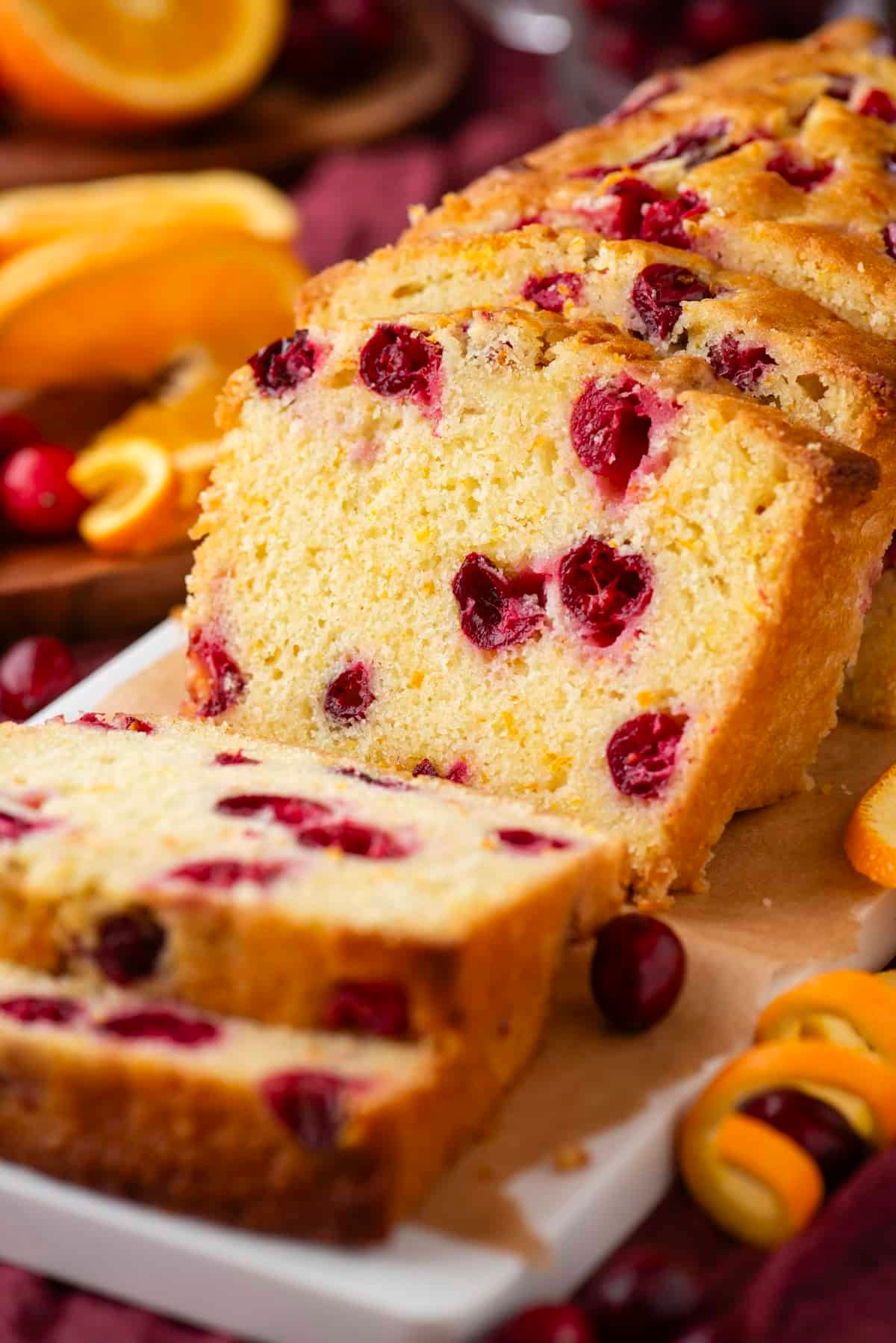 Vibrant cranberry orange bread loaf on a rustic wooden board, sliced, with fresh orange zest and cranberries scattered