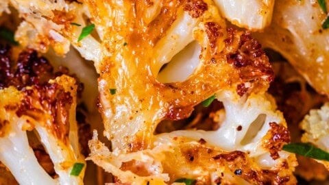 Close-up of golden brown, crispy garlic roasted cauliflower florets on a baking sheet, with fresh parsley garnish