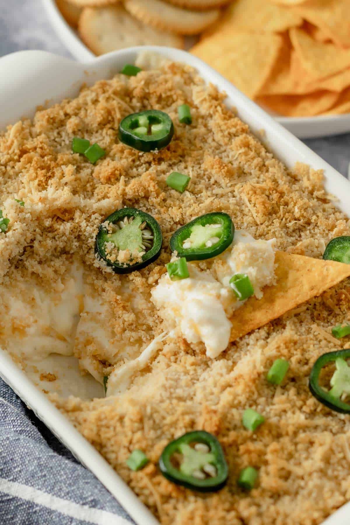 Delicious cheesy baked jalapeño popper dip in a rustic serving dish with crackers, bright lighting