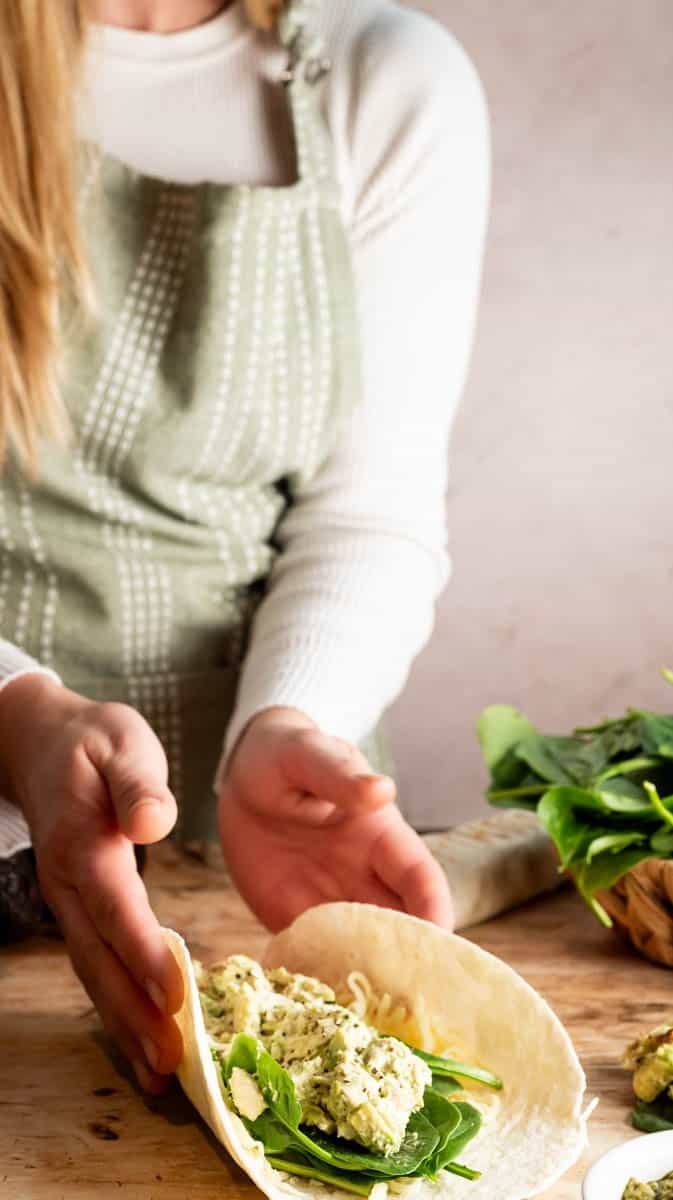 woman preparing creamy chicken spinach wraps in a kitchen