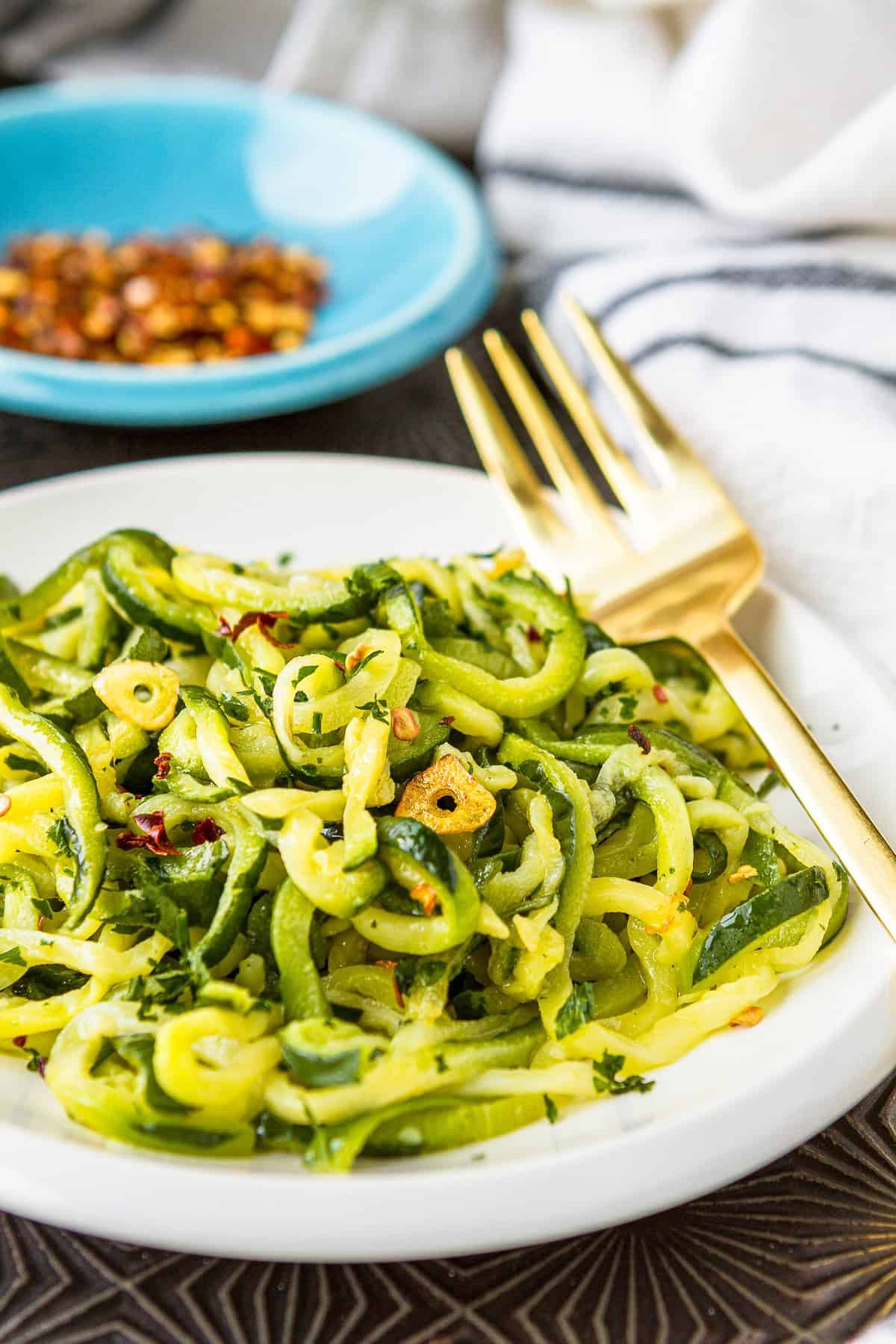 Vibrant close-up of zucchini noodles tossed with glistening garlic oil and fresh parsley in a rustic bowl