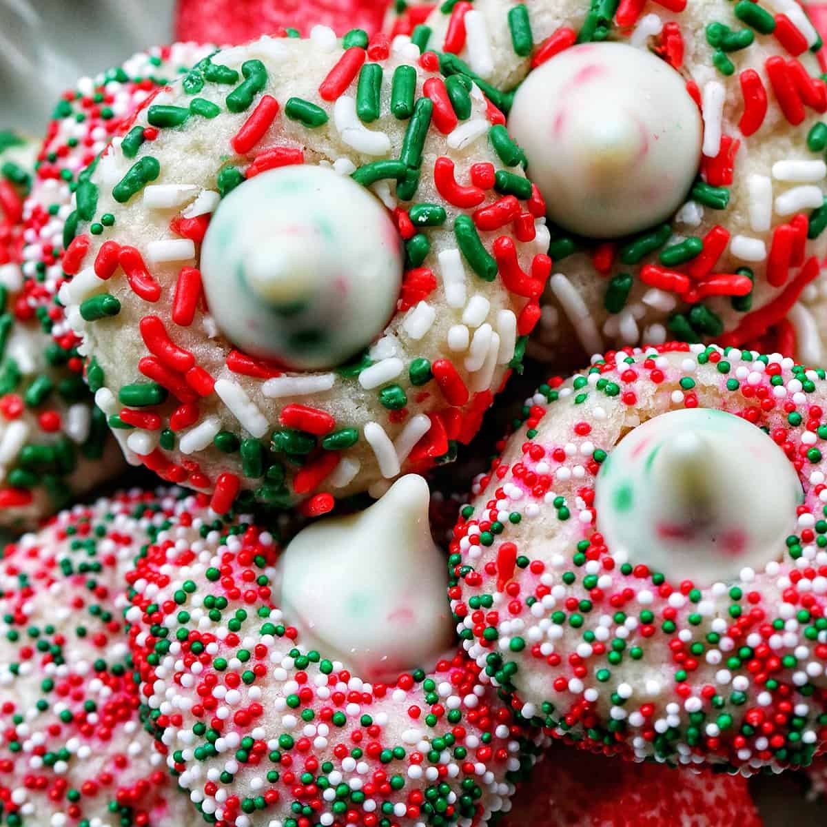 beautifully decorated Christmas french tip almond cookies with glossy white icing and festive sprinkles on a holiday platter