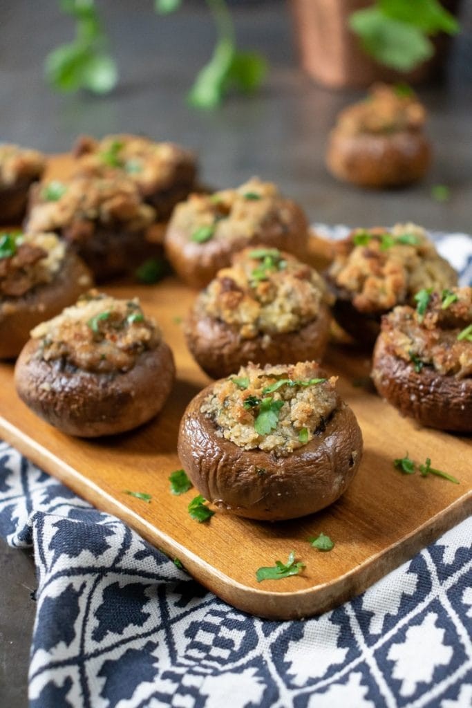 Close up photo of baked stuffed mushrooms with garlic herb filling on a rustic wooden board, garnished with fresh parsley.