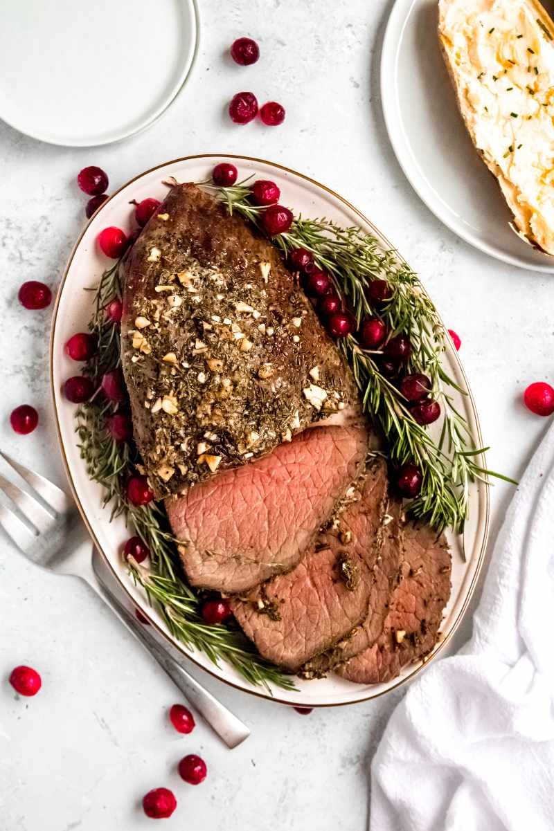 succulent garlic butter holiday roast beef with fresh rosemary and thyme on a platter, festive table setting, close-up