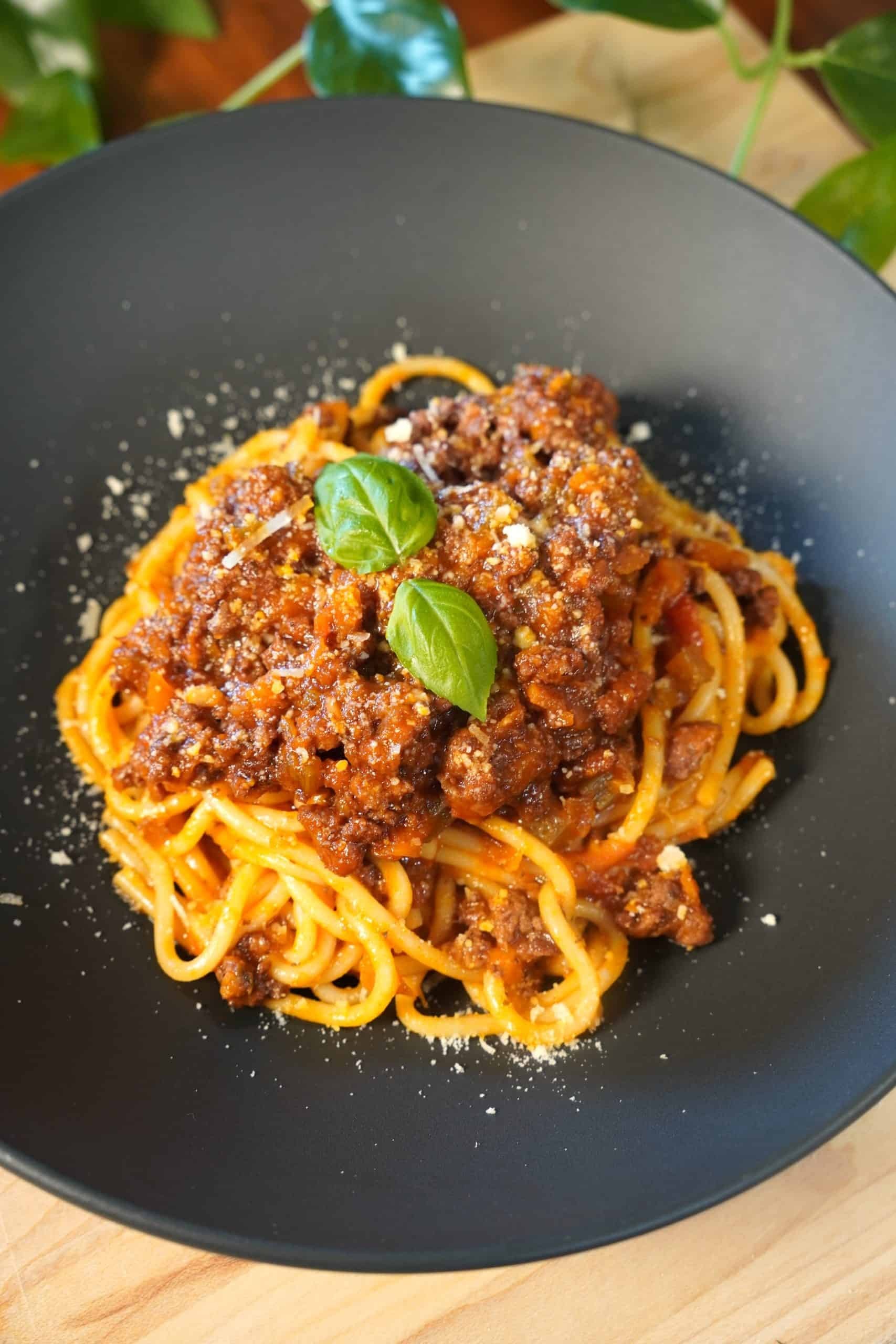 Delicious ground beef marinara pasta in a large bowl, garnished with fresh basil and parmesan cheese, on a rustic wooden table