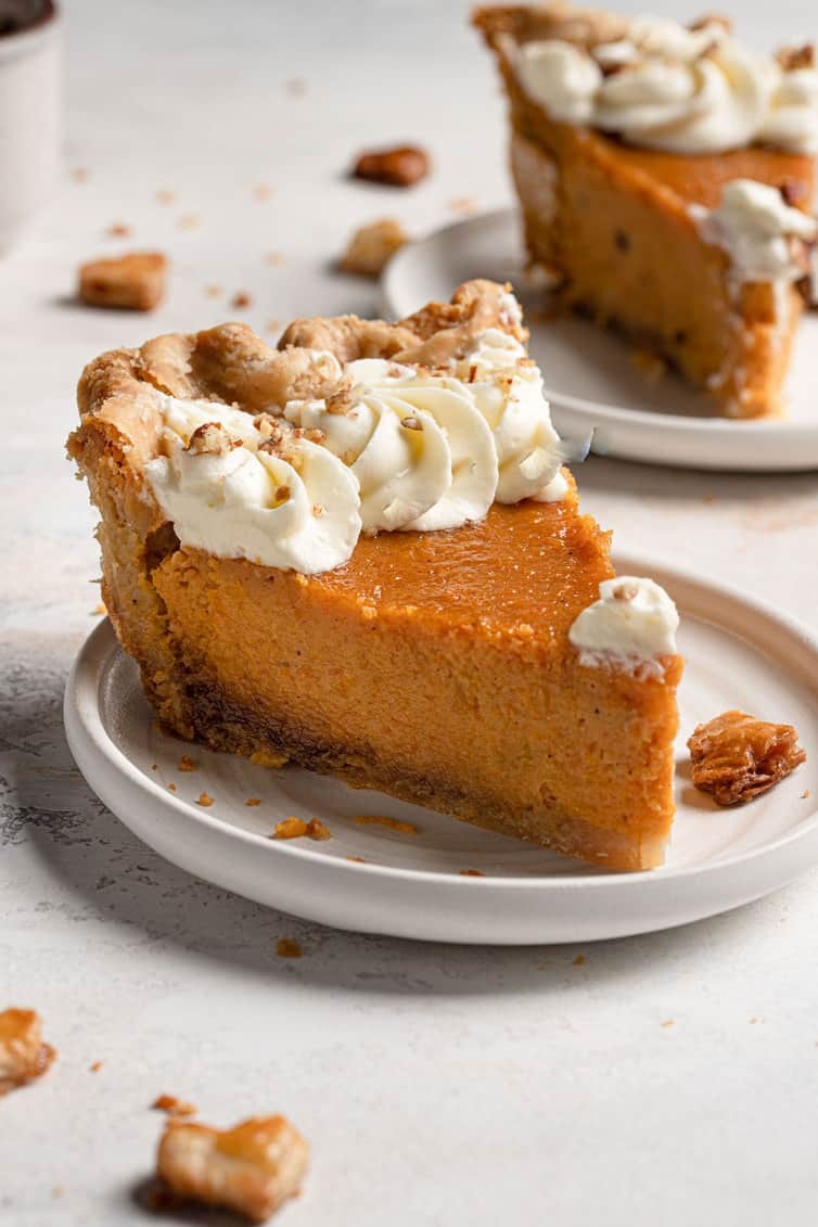Homemade sweet potato pie with a smooth, golden-brown top, a slice removed showing creamy filling, garnished with a dollop of whipped cream on a rustic wooden table