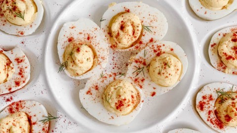 Close-up, vibrant deviled eggs with fresh dill and a sprinkle of paprika on a rustic wooden board, natural light