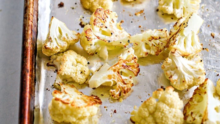 Close-up of golden brown garlic roasted cauliflower florets on a baking sheet, steam rising slightly